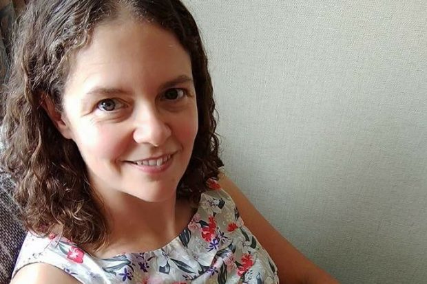 Picture of Julia sitting in a chair, wearing a floral top. Julia has curly, shoulder length brown hair. 