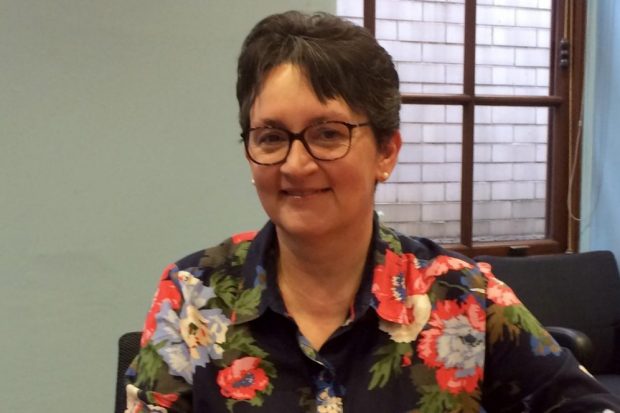 Picture of Janet who is wearing a flowery, navy blue shirt and round glasses. 