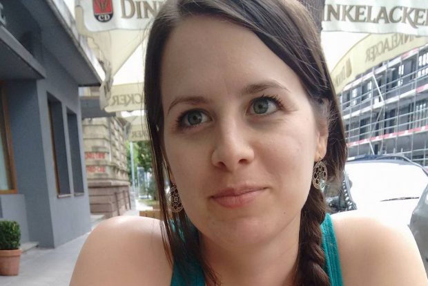 Picture of Nastassja sitting outside a cafe. Her dark brown hair is in a plait and she is looking to her right.