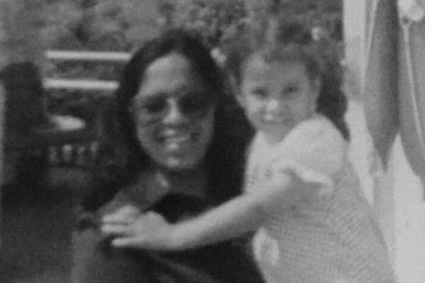 Grainy black and white photograph of a young Gemma being carried by her mother