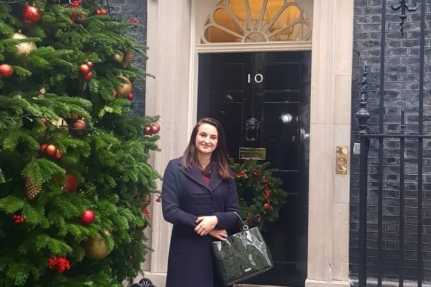 Picture of Emily standing in front of 10 Downing Street and next to a Christmas tree