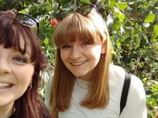 Picture of Louise and a friend in a garden. They are both wearing sunglasses on top of their head. 