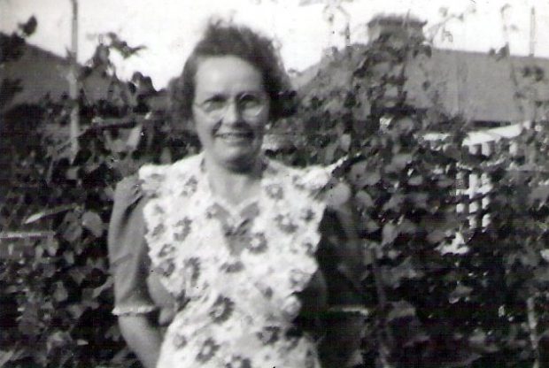 Black and white photograph of Alis grandmother Florence. Florence is standing in a garden wearing a floral pinafore