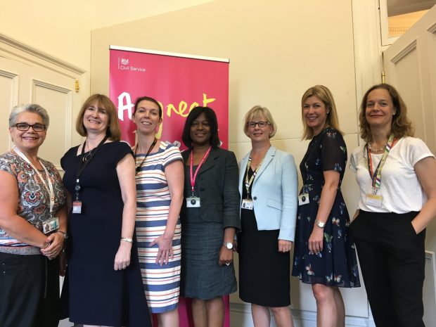 The HMRC Executive Committee posing in their office, standing in front of a Civil Service banner saying "A great place to work"